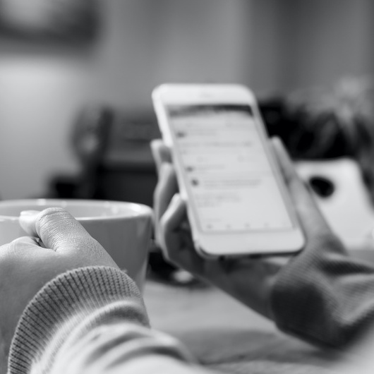 Dreamin Social - woman's hands holding white coffee cup and mobile phone while using social media in modern loft cafe